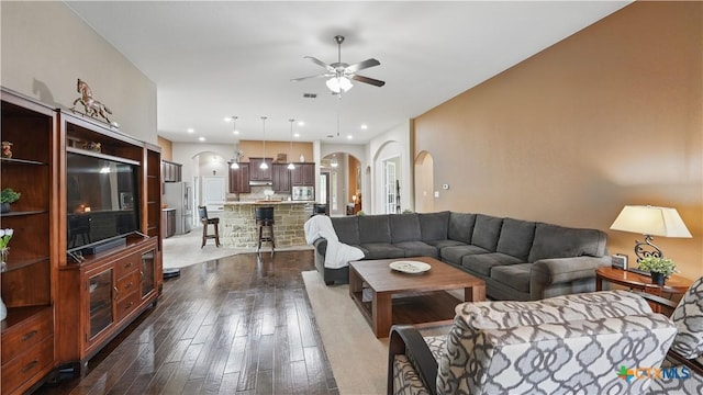 living area featuring arched walkways, a ceiling fan, and dark wood-style floors