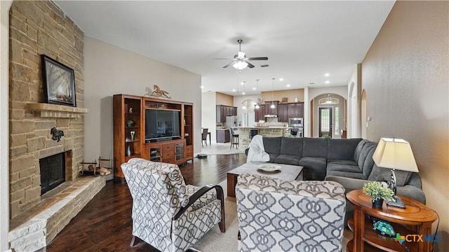 living room with ceiling fan, a fireplace, dark wood finished floors, and arched walkways