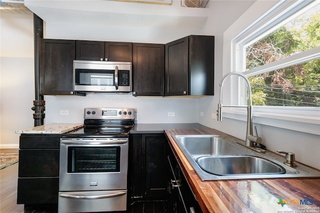 kitchen with stainless steel appliances, butcher block counters, dark brown cabinetry, sink, and light hardwood / wood-style flooring