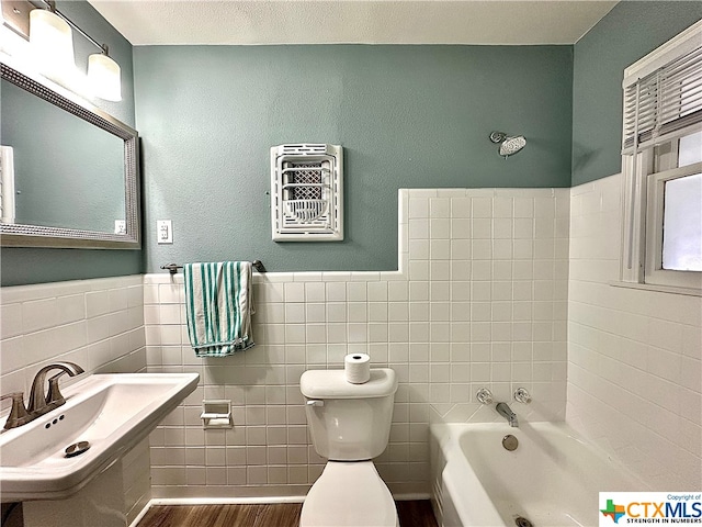 bathroom with tile walls, a bathing tub, hardwood / wood-style flooring, and toilet