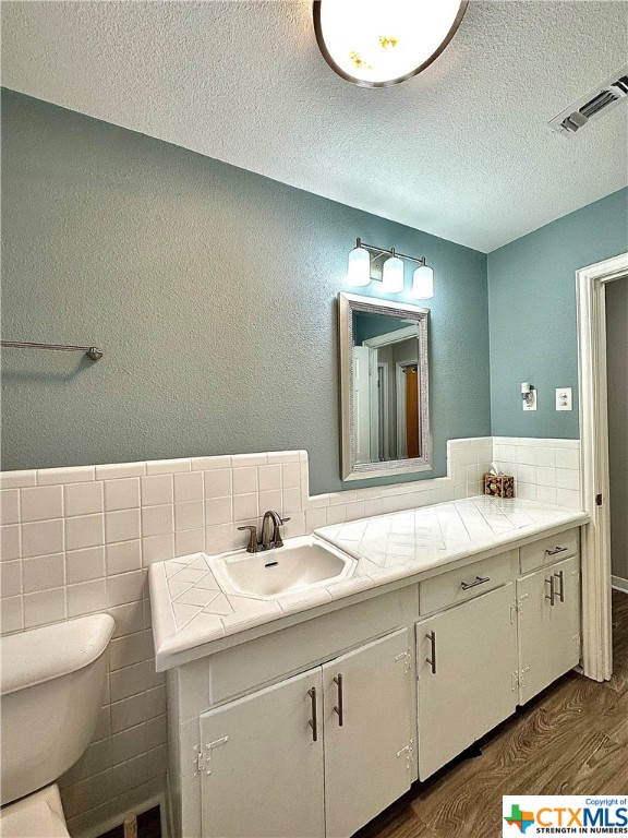 bathroom with toilet, tile walls, a textured ceiling, hardwood / wood-style flooring, and vanity