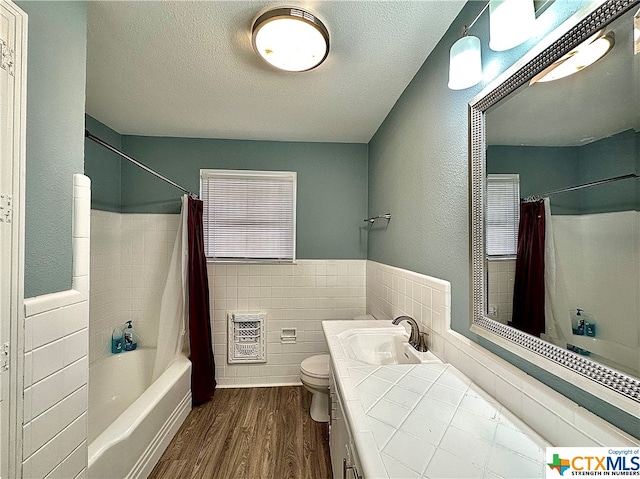 full bathroom featuring hardwood / wood-style flooring, heating unit, a textured ceiling, vanity, and tile walls