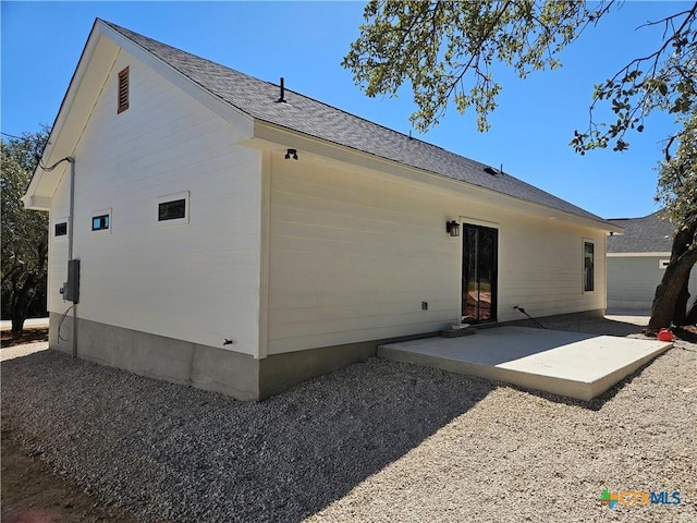 rear view of house with a shingled roof and a patio