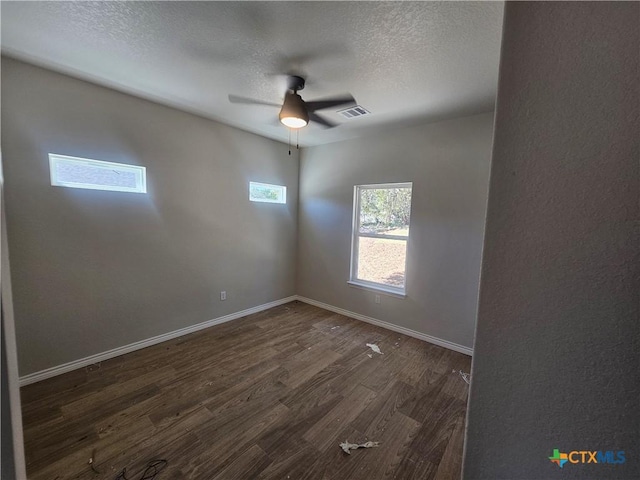 empty room with a textured ceiling, ceiling fan, dark wood-type flooring, visible vents, and baseboards