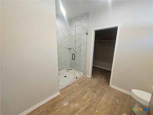 full bathroom featuring a stall shower, a spacious closet, baseboards, and wood finished floors