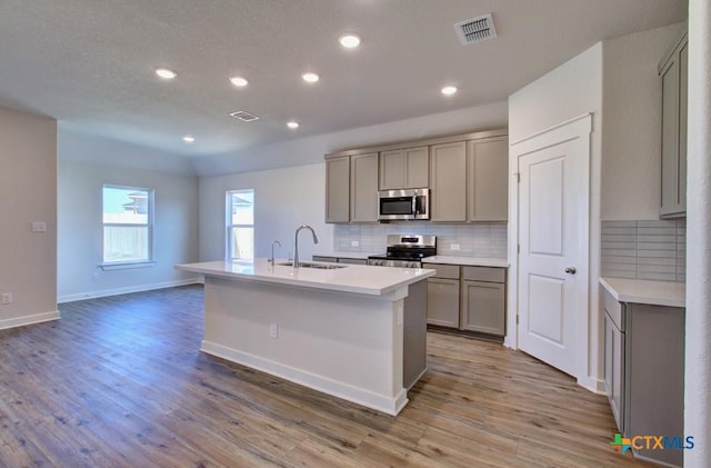 kitchen with visible vents, backsplash, gray cabinets, stainless steel appliances, and a sink