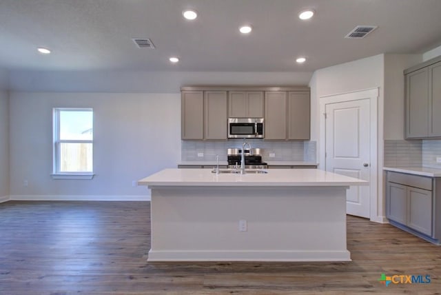 kitchen featuring visible vents, a sink, gray cabinetry, appliances with stainless steel finishes, and a kitchen island with sink