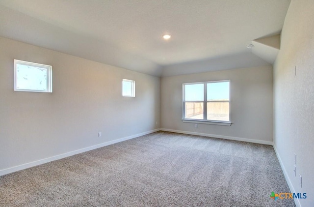 carpeted empty room featuring vaulted ceiling, baseboards, and a wealth of natural light