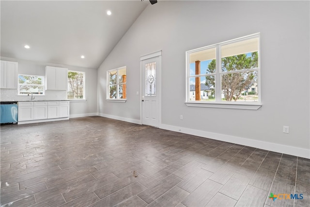 unfurnished living room with a wealth of natural light, dark hardwood / wood-style flooring, and high vaulted ceiling