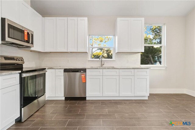 kitchen featuring white cabinets, stainless steel appliances, vaulted ceiling, and light stone counters