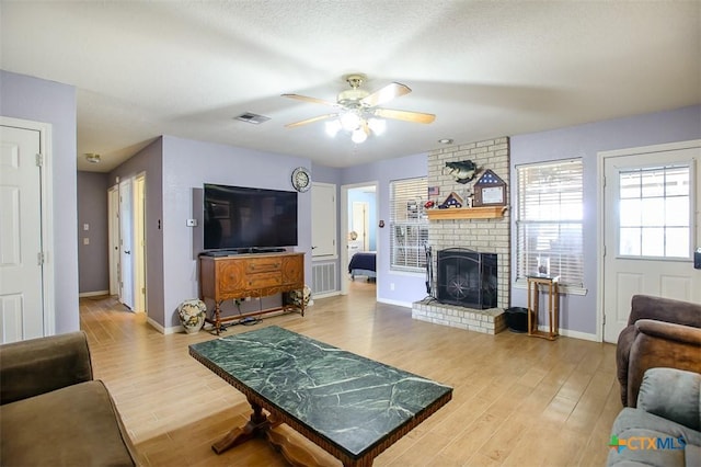 living area featuring wood finished floors, visible vents, baseboards, a fireplace, and ceiling fan