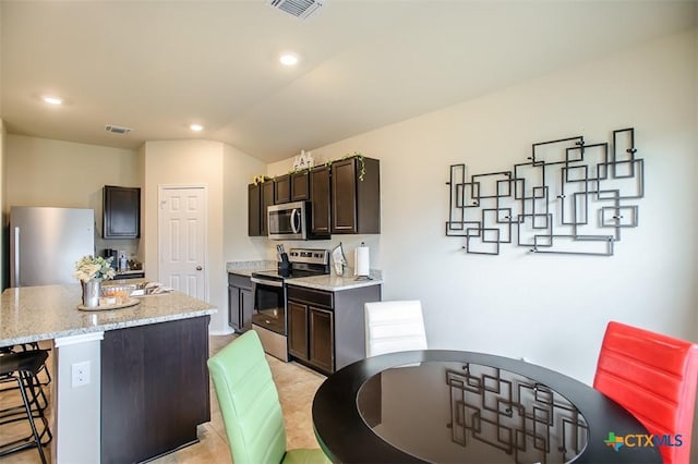 kitchen featuring dark brown cabinets, visible vents, a kitchen island, appliances with stainless steel finishes, and a breakfast bar area