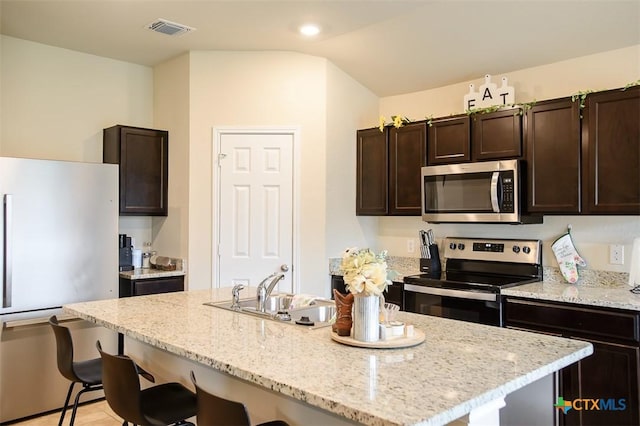 kitchen featuring a kitchen bar, dark brown cabinetry, appliances with stainless steel finishes, and a sink