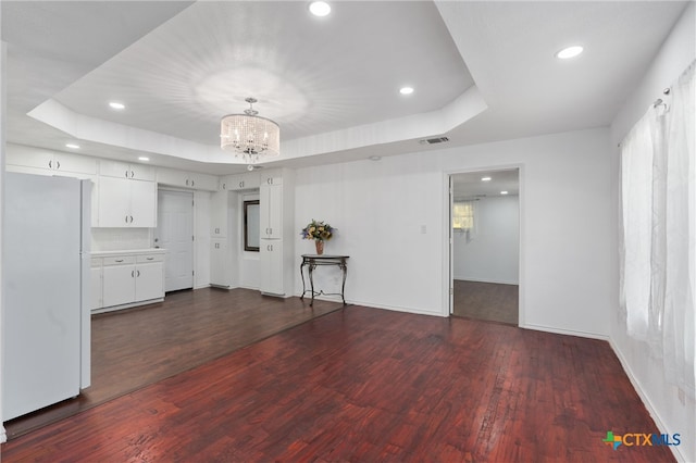 unfurnished living room featuring plenty of natural light, a raised ceiling, dark hardwood / wood-style flooring, and a notable chandelier