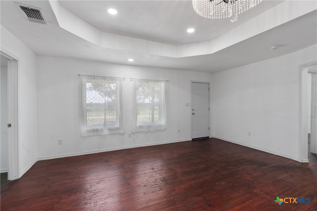 empty room with dark hardwood / wood-style flooring, a chandelier, and a tray ceiling