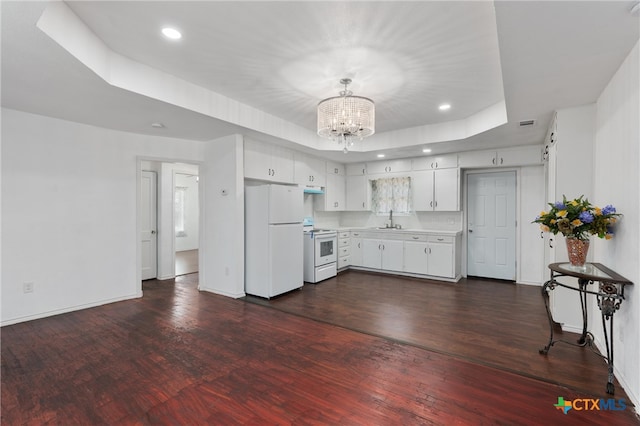 kitchen with a tray ceiling, white appliances, a notable chandelier, white cabinets, and dark hardwood / wood-style flooring