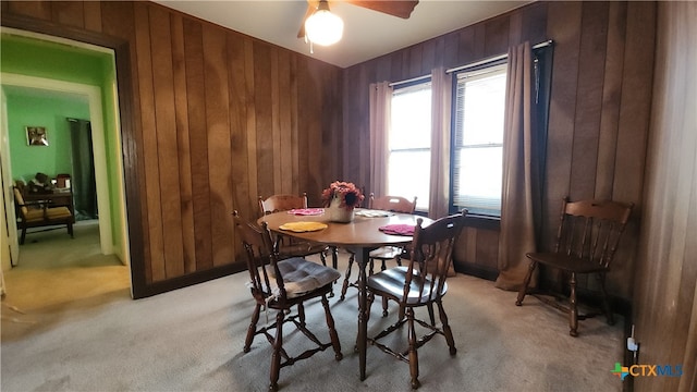 carpeted dining area with ceiling fan and wooden walls