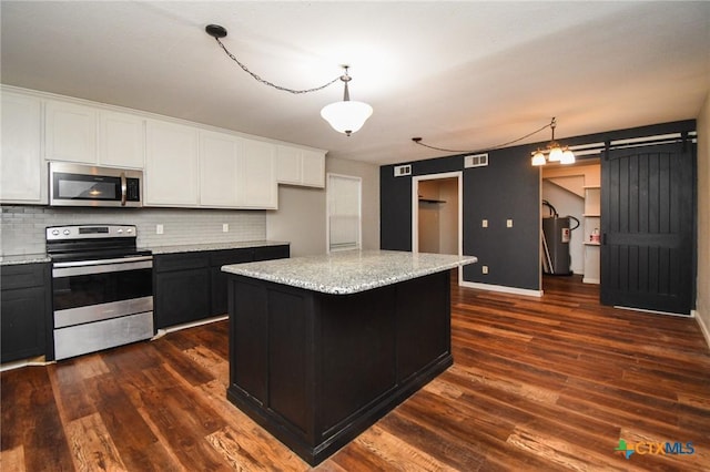 kitchen featuring appliances with stainless steel finishes, decorative light fixtures, a kitchen island, a barn door, and white cabinetry