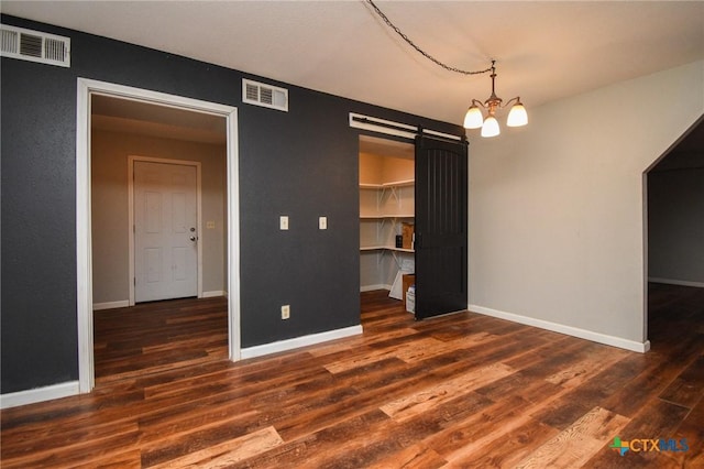 unfurnished bedroom with a closet, an inviting chandelier, a spacious closet, dark hardwood / wood-style floors, and a barn door