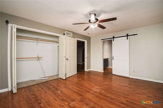 unfurnished bedroom with ceiling fan, a closet, dark hardwood / wood-style flooring, and a barn door