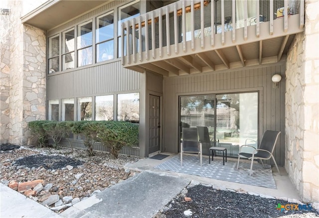 view of exterior entry featuring a patio area, stone siding, and a balcony