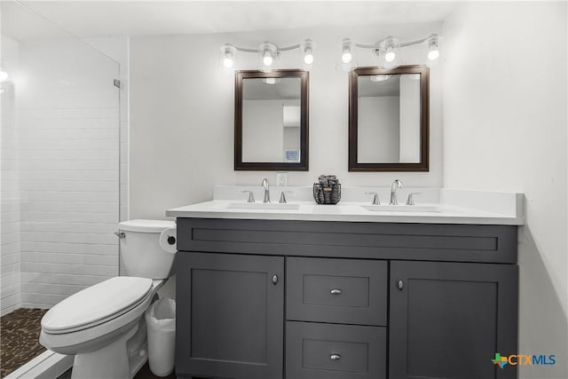 full bath featuring double vanity, a tile shower, toilet, and a sink