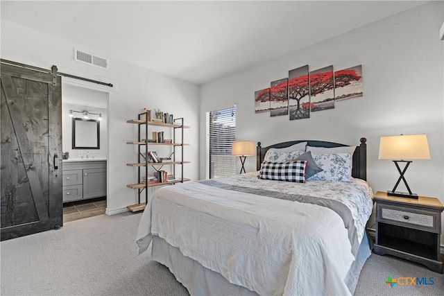 carpeted bedroom with ensuite bath, a barn door, baseboards, and visible vents