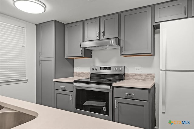 kitchen with under cabinet range hood, gray cabinets, stainless steel electric range oven, and freestanding refrigerator