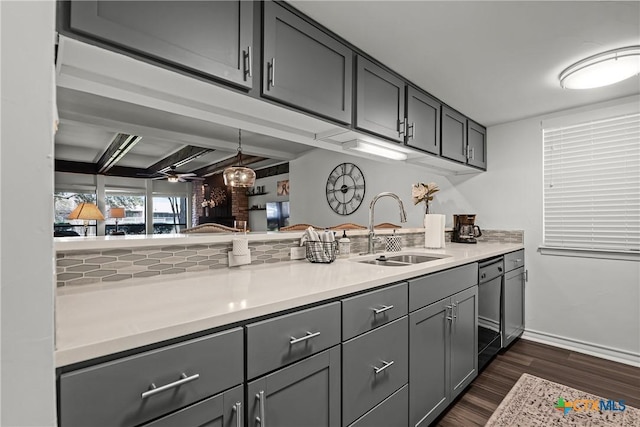 kitchen with dishwashing machine, gray cabinets, dark wood-style flooring, a sink, and light countertops