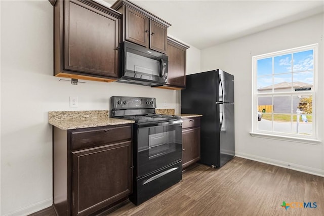 kitchen with hardwood / wood-style flooring, light stone countertops, dark brown cabinets, and black appliances