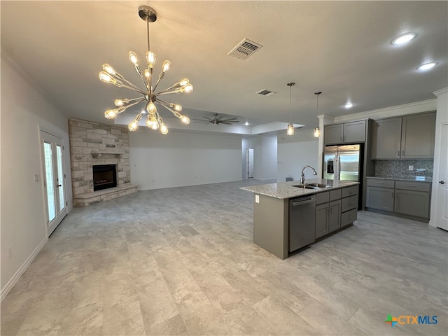 kitchen featuring ceiling fan with notable chandelier, stainless steel appliances, a center island with sink, gray cabinets, and a fireplace