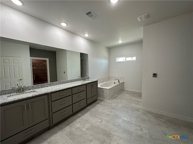 bathroom with vanity, a textured ceiling, and a relaxing tiled tub