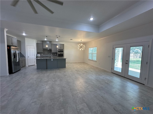 kitchen with a center island with sink, gray cabinetry, crown molding, backsplash, and appliances with stainless steel finishes