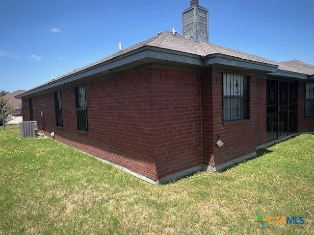 view of side of home featuring central AC unit and a lawn