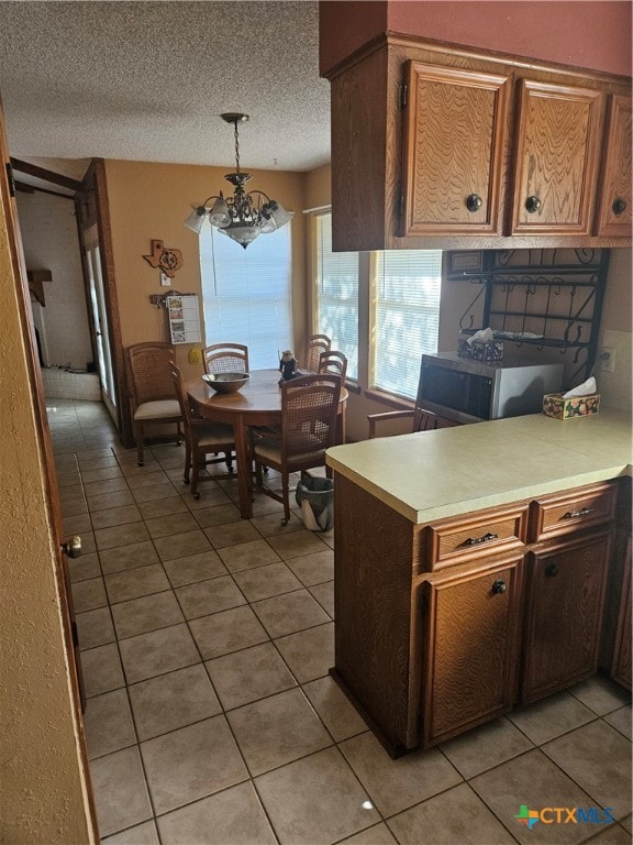 kitchen with hanging light fixtures, light tile patterned floors, a textured ceiling, kitchen peninsula, and a chandelier