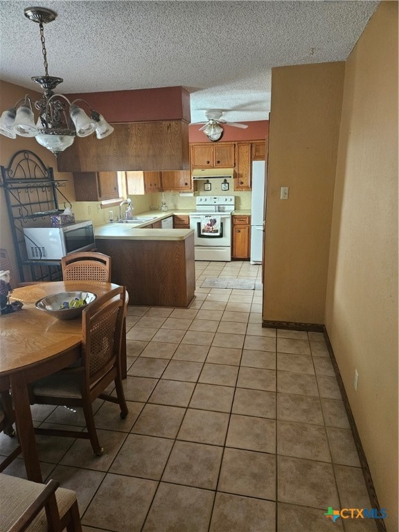 kitchen featuring white appliances, ceiling fan with notable chandelier, hanging light fixtures, light tile patterned flooring, and kitchen peninsula