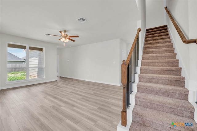 stairs with wood finished floors, visible vents, a ceiling fan, and baseboards