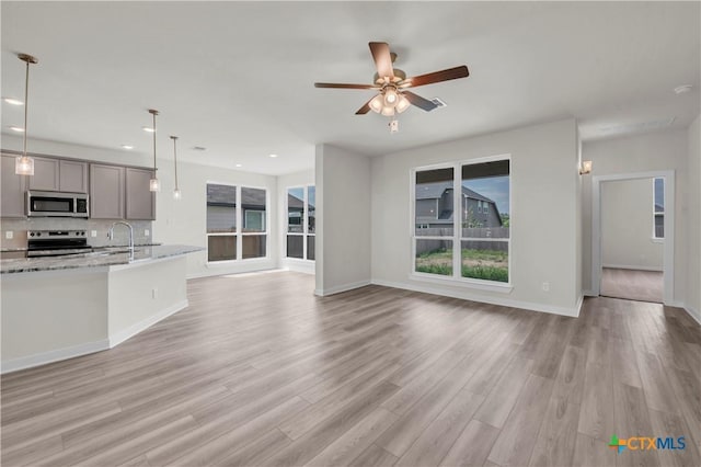 unfurnished living room with a ceiling fan, a sink, light wood finished floors, baseboards, and recessed lighting