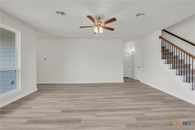 unfurnished living room featuring light wood-style floors, visible vents, a ceiling fan, and stairs