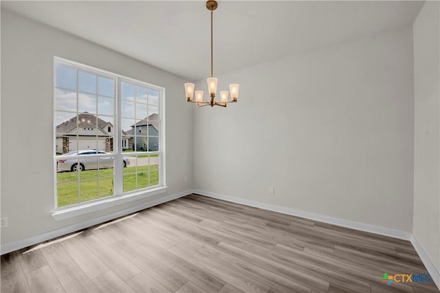 unfurnished dining area featuring baseboards, a notable chandelier, and wood finished floors