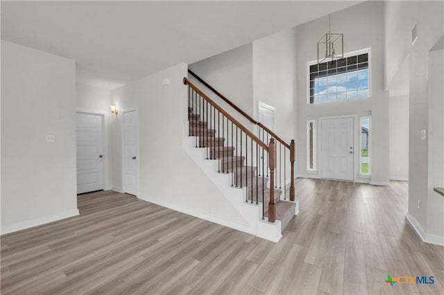 entryway with baseboards, visible vents, a towering ceiling, light wood-style floors, and stairway