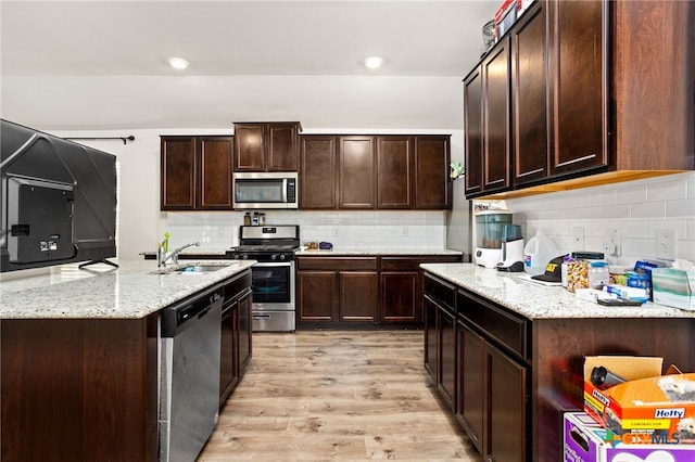 kitchen with stainless steel appliances, decorative backsplash, dark brown cabinetry, sink, and light wood-type flooring