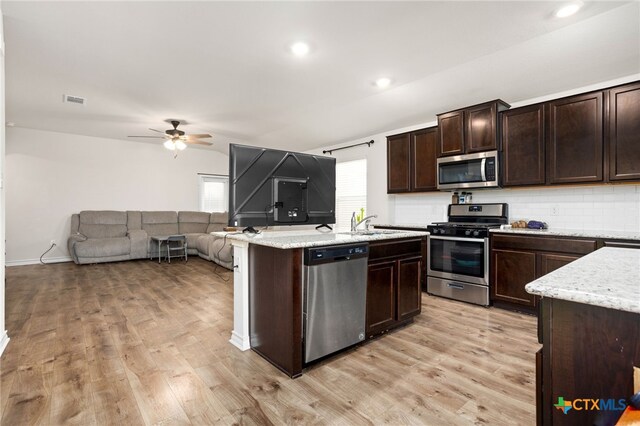 kitchen featuring stainless steel appliances, decorative backsplash, ceiling fan, dark brown cabinets, and light wood-type flooring