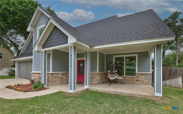 exterior space featuring fence, roof with shingles, stone siding, a porch, and driveway