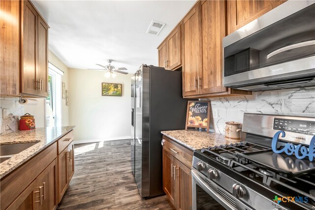 kitchen featuring ceiling fan, stainless steel appliances, light stone counters, dark hardwood / wood-style flooring, and backsplash