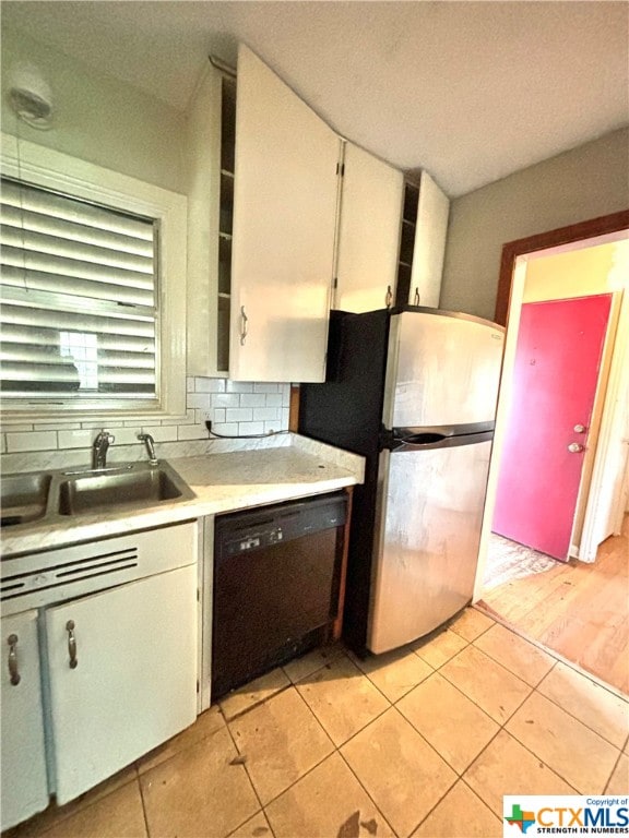 kitchen featuring stainless steel fridge, black dishwasher, sink, decorative backsplash, and white cabinets