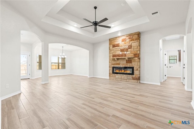 unfurnished living room with ceiling fan, a tray ceiling, light hardwood / wood-style floors, and a stone fireplace