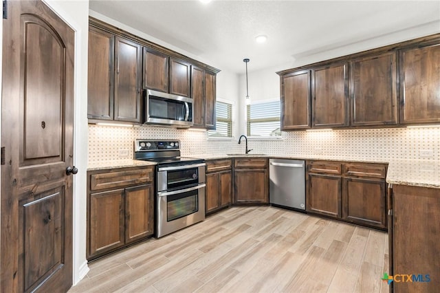 kitchen with sink, appliances with stainless steel finishes, light stone countertops, decorative light fixtures, and light wood-type flooring