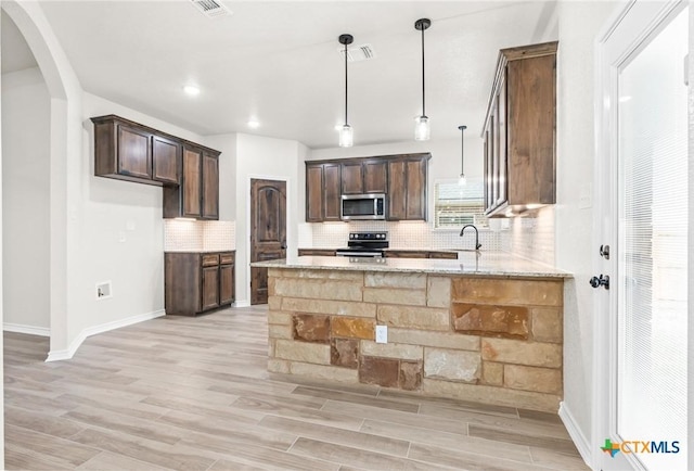 kitchen featuring light hardwood / wood-style flooring, appliances with stainless steel finishes, hanging light fixtures, dark brown cabinets, and light stone countertops