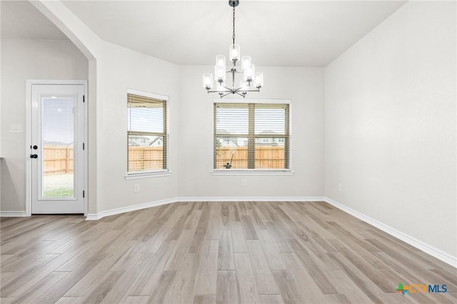 spare room with an inviting chandelier, a wealth of natural light, and light hardwood / wood-style floors